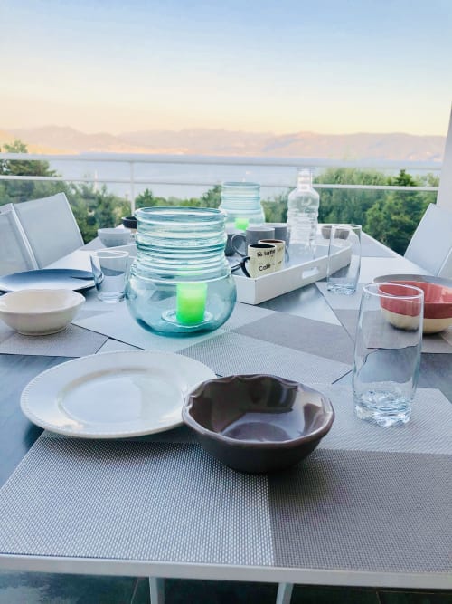 Elegant outdoor dining table on Corsican villa terrace overlooking sea at sunset with place settings and water glasses