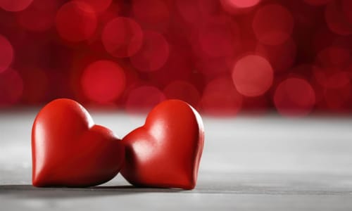 Two red heart shapes on white surface with blurred red bokeh background at Château d'Hassonville B&B