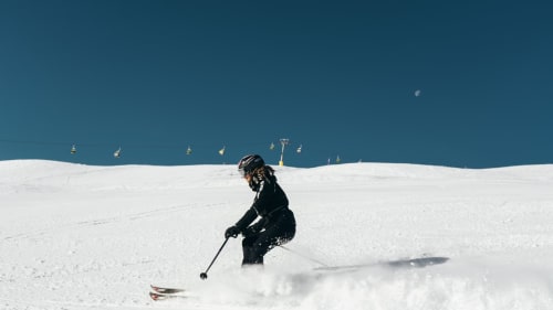 Skieur descendant une pente enneigée près de La Petite étoile, Saint-Dalmas-le-Selvage, sous ciel bleu avec remontées mécaniques