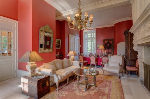 Elegant salon at Château d'Alexis de Tocqueville with coral walls, cream sofa, gilt mirror, and chandelier in Tocqueville,