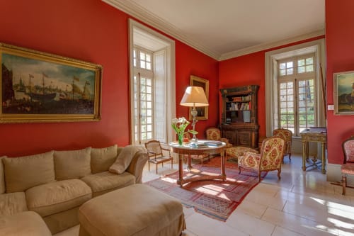Elegant red salon at Château d'Alexis de Tocqueville with period furniture, classical paintings, and natural light from