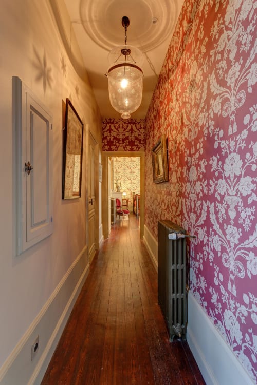 Elegant hallway at Château d'Alexis de Tocqueville with damask wallpaper, pendant light, and hardwood floors.