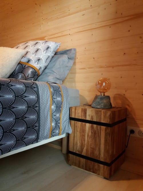 Cozy glamping bedroom at Belloréade with wooden ceiling, patterned bedding, and rustic nightstand with amber lamp