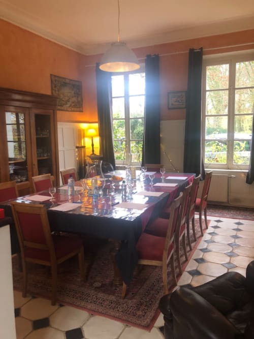 Élégante salle à manger de La Tour Blanche avec table drapée de noir, chaises rouges et hautes fenêtres donnant sur Forest-Montiers