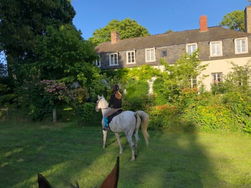 Hôte équestre montant un cheval gris à La Tour Blanche, maison d'hôtes à Forest-Montiers, France, avec maison couverte de lierre et jardins