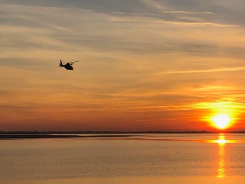 Silhouette d'hélicoptère militaire au coucher de soleil sur les eaux calmes près de La Tour Blanche, Forest-Montiers