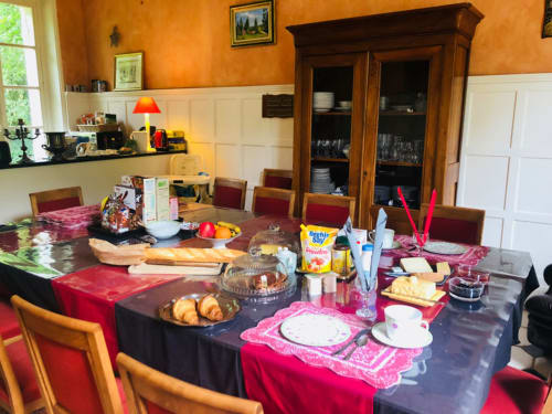 Salle à manger élégante du B&B La Tour Blanche aux murs orange, table dressée avec serviettes roses, meuble ancien et mobilier d'époque