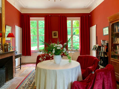 Élégant salon rouge à La Tour Blanche avec cheminée, table ronde fleurie et vue sur le jardin