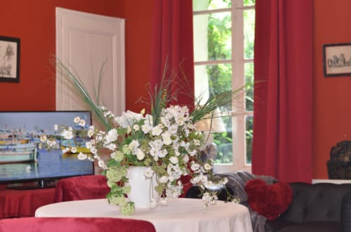 Élégant salon rouge de la Maison d'hôtes La Tour Blanche avec composition florale blanche, rideaux rouges et vue sur le jardin