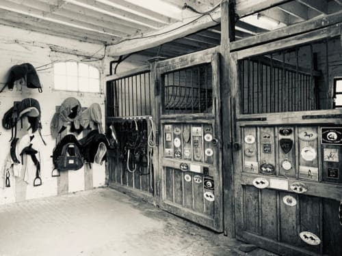 Intérieur rustique de l'écurie à La Tour Blanche avec box pour chevaux, rangements de sellerie et plaques vintage sur portes en bois.