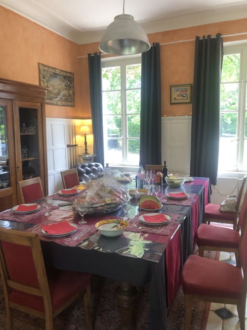Élégante salle à manger de la Maison d'hôtes La Tour Blanche avec table dressée en rose, sets de table rouges et hautes fenêtres à Forest-Montiers
