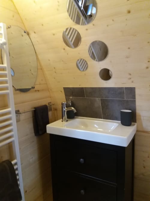 Modern bathroom in Belloréade glamping bergerie with white sink, black vanity, dark tile backsplash, and wooden ceiling with