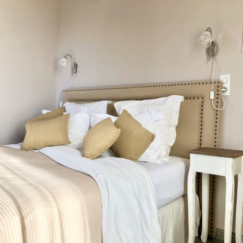 Beige upholstered bed with white linens and tan pillows at Villas Marincelu villa in Corsica