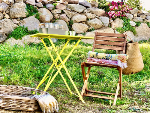 Outdoor seating area at Casa Serena villa with yellow table, wooden chair with cushions, wicker basket, and stone wall with