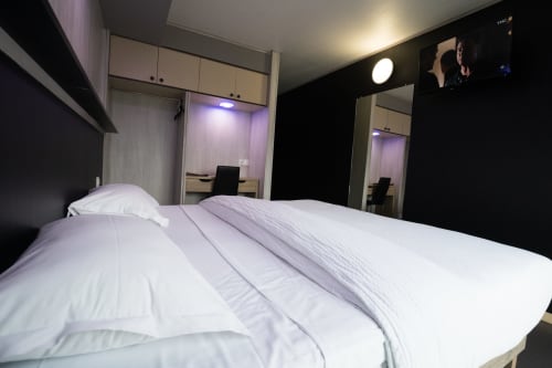 Habitació moderna de l'Hôtel Rocade a Pamiers amb roba de llit blanca, armari espill i il·luminació ambiental