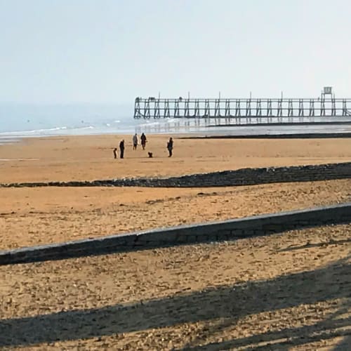 Des visiteurs marchent sur la plage de sable fin près de Port-en-Bessin, avec une historique jetée en arrière-plan