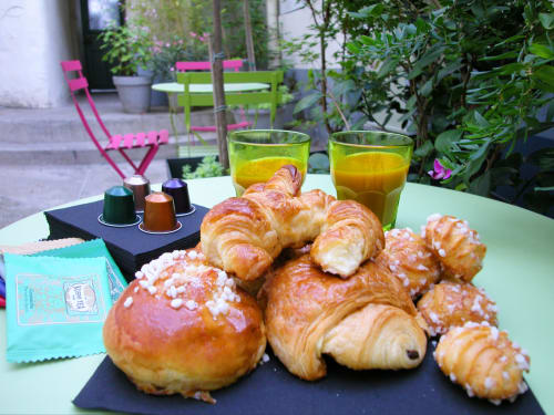 Parisian breakfast spread with croissants, pastries, fresh juice, and coffee pods on a patio at Montmartre Romantic B&B