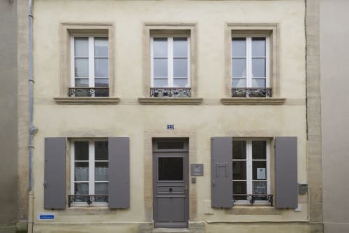 Cremefarbene Fassade von Les Filles du Bord de Mer in Port-en-Bessin mit grauen Fensterläden und verziertem Schmiedeeisen-Balkon