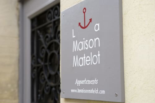 Schild des Aparthotels La Maison Matelot mit rotem Ankerlogo in Port-en-Bessin, Frankreich