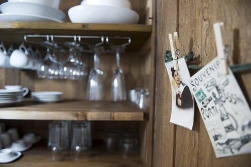 Étagères rustiques en bois dans l'appartement Les Filles du Bord de Mer présentant de la verrerie, de la vaisselle blanche et des cartes postales vintage