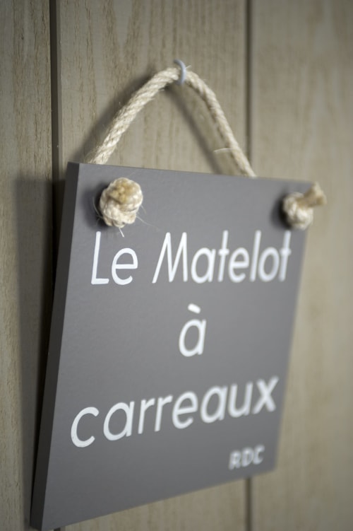 Enseigne grise suspendue « Le Matelot à carreaux » avec poignée en corde sur mur en bois à l'hôtel Les Filles du Bord de Mer