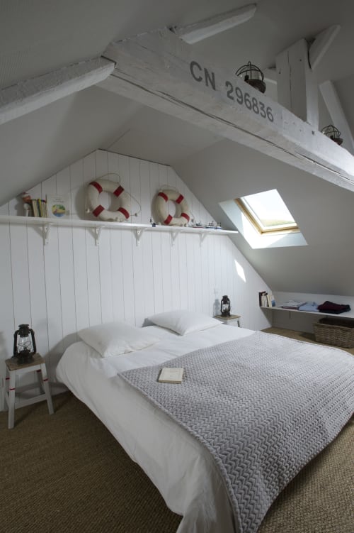 Chambre mansardée au thème nautique aux Filles du Bord de Mer : lit blanc, bouées, lucarne et décoration portuaire
