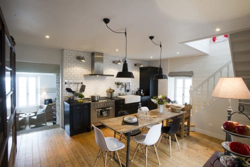 Moderne keuken-eetruimte met zwarte hanglantaarns, witte tegels, houten eettafel en zeezicht bij Les Filles du Bord