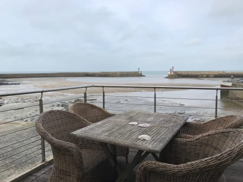 Mobilier en rotin sur une terrasse vue mer surplombant le port de Port-en-Bessin à marée basse