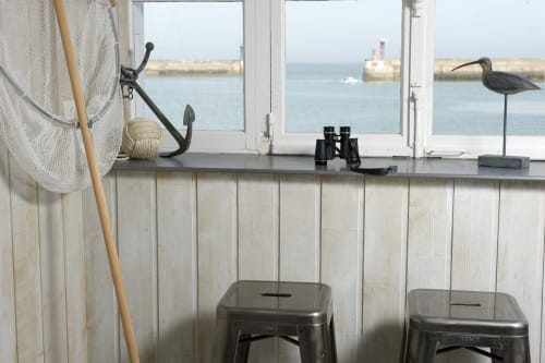 Fenêtre de chaumière côtière vue sur le port, filet de pêche, jumelles et tabourets en métal dominant Port-en-Bessin-Huppain.