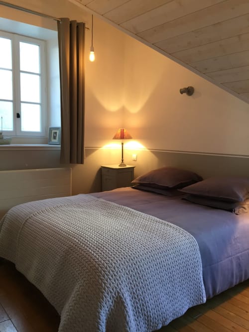 Gezellige slaapkamer in het huisje Les Filles du Bord de Mer met twee eenpersoonsbedden, warm licht en zeezicht vanuit het raam in Port-en-Bessin