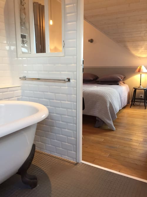 Badkamer met witte metrotegels en vrijstaand bad, aangrenzende slaapkamer met bed en lamp bij Les Filles du Bord de