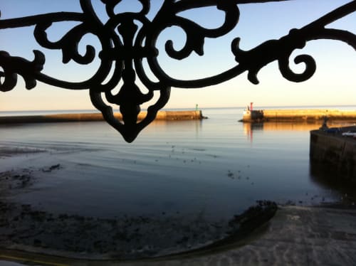 Sierlijk gesmeed ijzeren reling omlijst het serene havenaussicht van Port-en-Bessin met houten pieren en rustig water