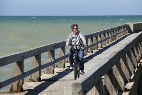 Cycliste sur la jetée côtière de Port-en-Bessin admirant la vue marine près de l'hôtel Les Filles du Bord de Mer