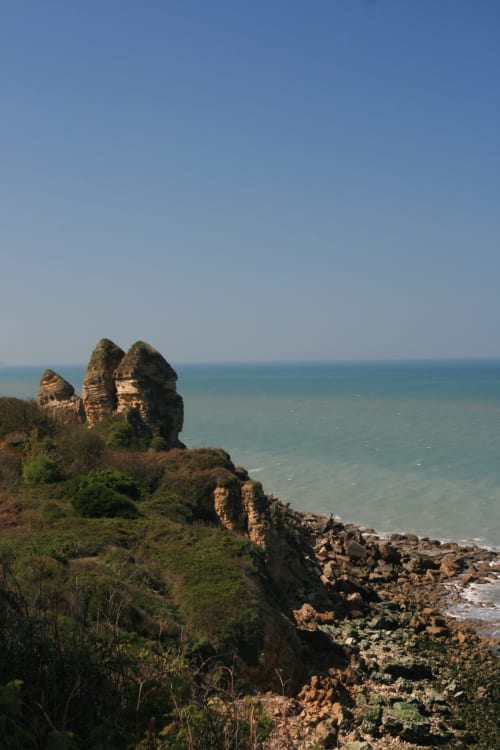 Formations rocheuses dramatiques surplombant les eaux turquoise près de Les Filles du Bord de Mer à Port-en-Bessin