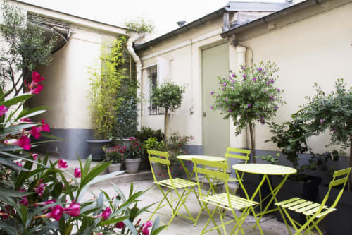 Charming patio courtyard at Montmartre Romantic B&B Paris with lime green chairs, blooming flowers, and ivy-covered walls