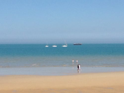 Plage de sable aux Filles du Bord de Mer avec baigneurs et voiliers dans les eaux turquoise de Port-en-Bessin