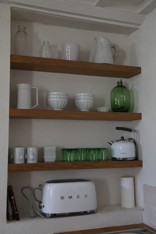 Étagères de cuisine avec vaisselle blanche, bouteilles en verre, bouteilles vintage vertes, bouilloire blanche et grille-pain SMEG aux Filles