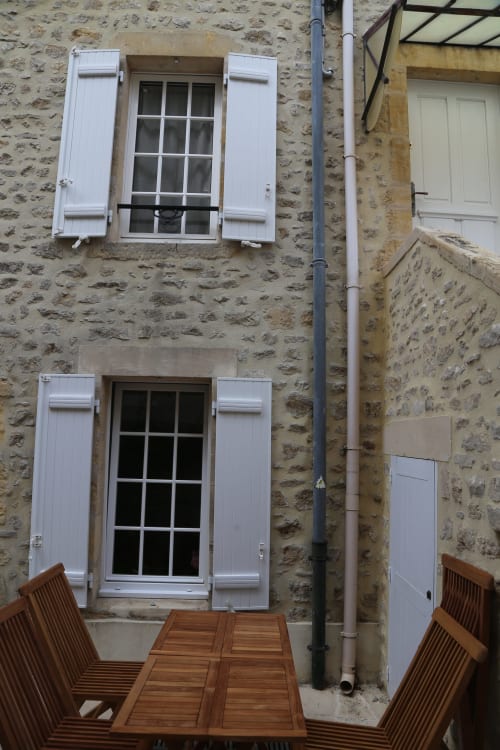 Cour de maison en pierre à Les Filles du Bord de Mer avec volets blancs et mobilier de jardin en bois