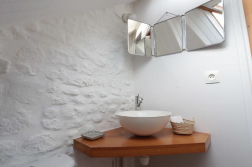 Lavabo minimaliste avec vasque blanche sur plan en bois, miroir encadré et murs en pierre blanche texturée à Les