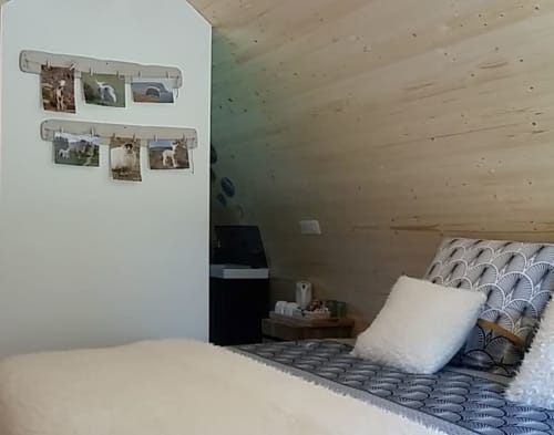 Cozy glamping bedroom at Belloréade with wooden ceiling, patterned bedding, white pillow, and photos hung on wall rail.
