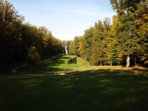 Fairway du parcours de golf avec drapeau numéroté à Un Air De Famille à Vittel, France, entouré d'arbres d'automne