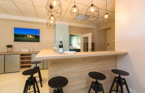 Élégant bar de l'hôtel Un Air De Famille Vittel avec comptoir en bois, tabourets noirs, luminaires géométriques et écran TV
