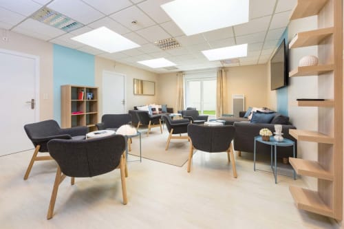 Espace lounge moderne au gîte Un Air De Famille à Vittel avec fauteuils noirs, étagères bois, télévision et vue sur le jardin