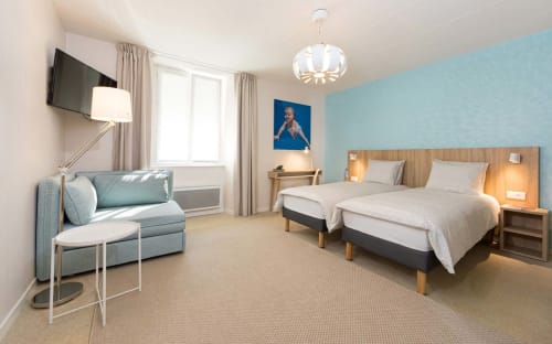 Chambre moderne à Un Air De Famille à Vittel avec lits jumeaux, coin détente, mur d'accent bleu clair et vue sur le jardin