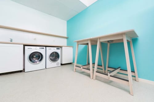 Buanderie moderne aux murs turquoise, lave-linges et sèche-linge frontaux, table à repasser en bois au gîte Côté Châtillon