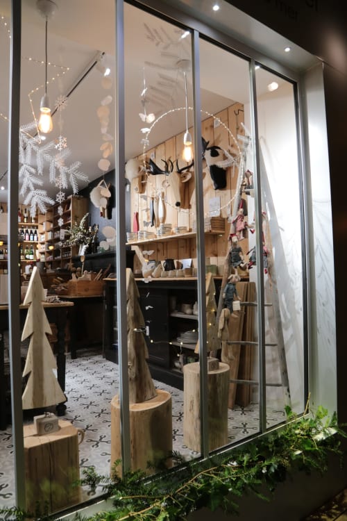 Vitrine de boutique aux thèmes festifs aux Filles du Bord de Mer à Port-en-Bessin avec cerfs en bois, luminaires suspendus et