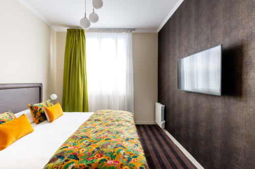 Modern studio bedroom at Hotel Residence Europe & Spa in Clichy with colorful bedding, wall-mounted TV, green curtains and