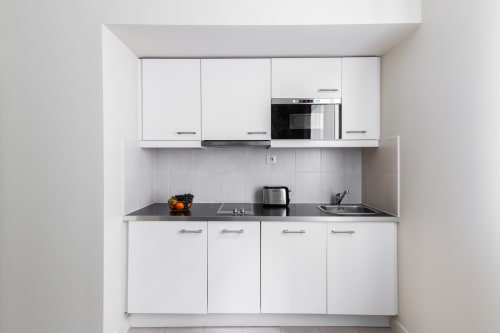 Modern white kitchen in Hotel Residence Europe studio apartment, Clichy, with built-in appliances and dark countertop