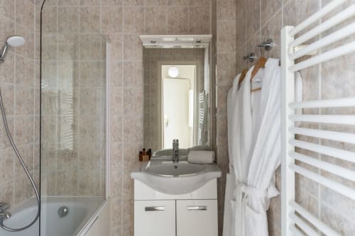 Modern studio bathroom at Hotel Residence Europe & Spa Clichy with white sink vanity, mirror, shower, heated towel rack and