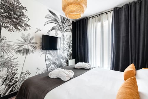 Modern bedroom at Hotel Residence Europe & Spa with tropical wallpaper, flat-screen TV, black curtains, and woven pendant